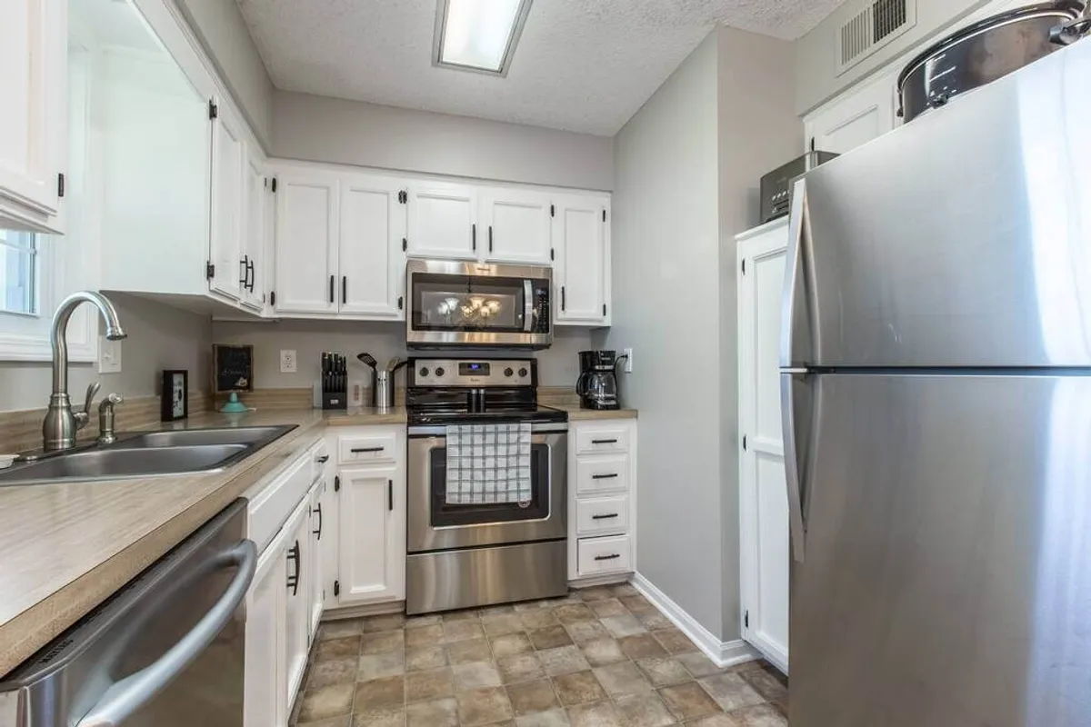 A second view of the kitchen, highlighting additional stainless steel appliances, white cabinetry, and a well-organized countertop with cooking utensils. The scene suggests an atmosphere ready for group cooking or baking sessions, and emphasizes the kitchen's modern, functional design.