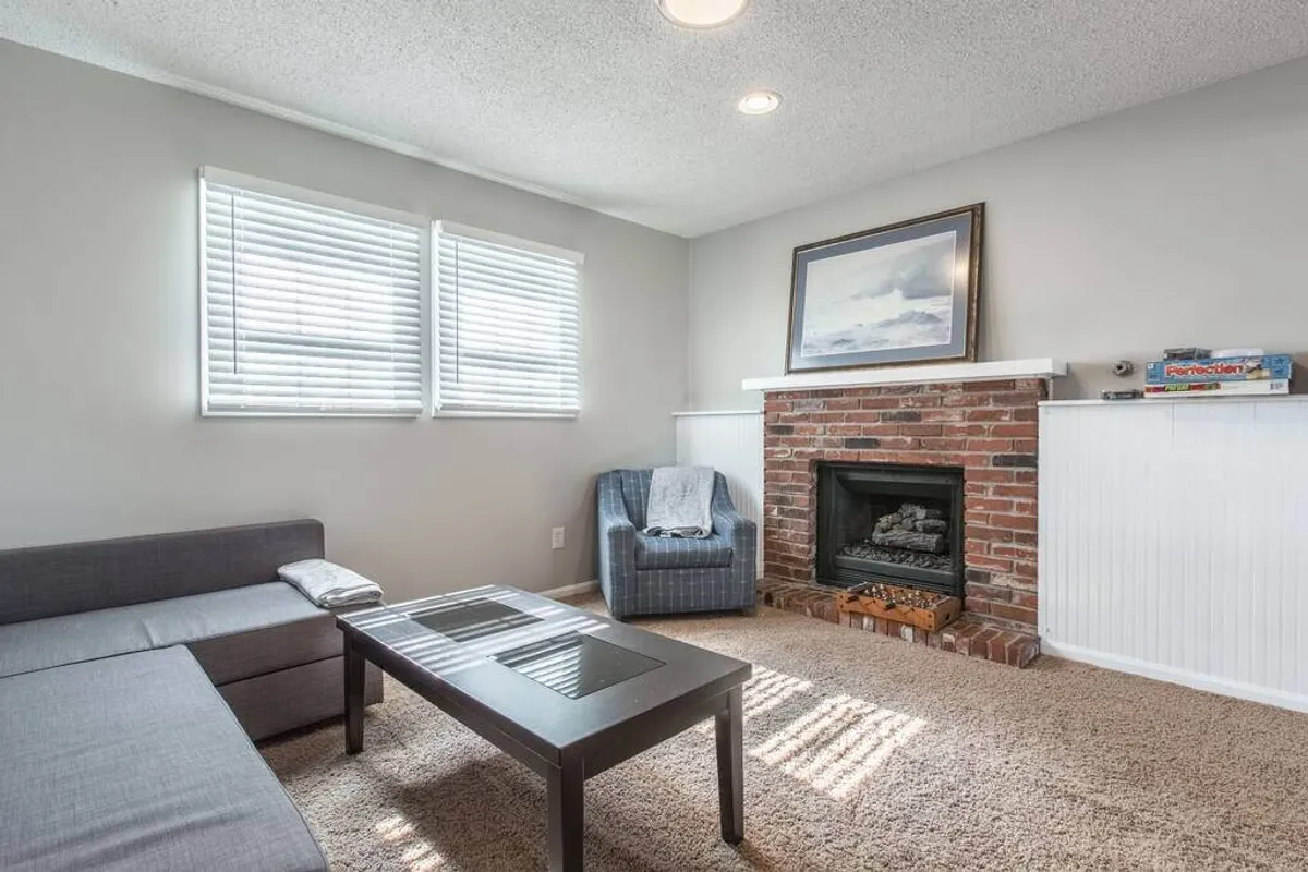 A stylish living area featuring a prominent fireplace, modern sofa, coffee table, and artistic wall décor. The ambiance is warm and calm, perfect for both focused work sessions and laid-back moments. The seating arrangement offers a conducive environment for reading or video calls.