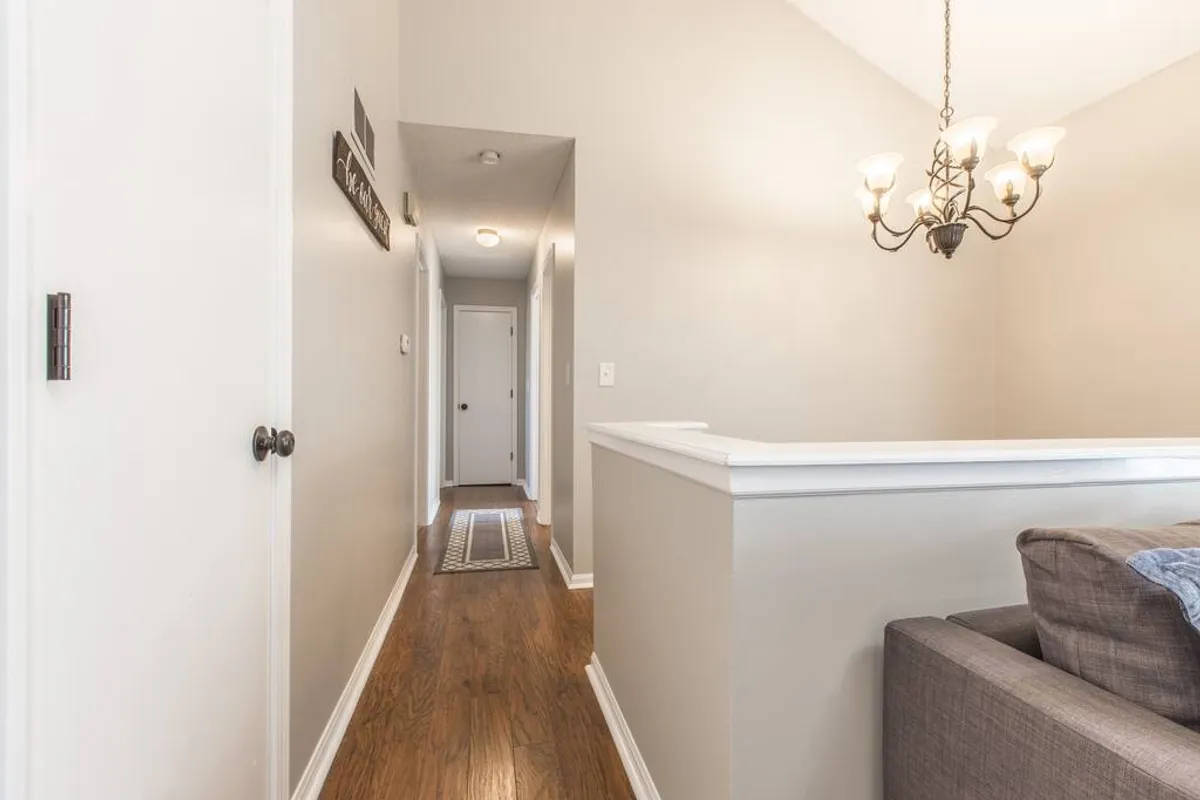 A bright hallway illuminated by an elegant chandelier leads the eye toward a welcoming seating area with a sofa. The space feels open and easy to navigate, ideal for greeting guests and moving about freely.